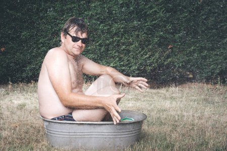 Foto de Hombre enfriamiento en bañera de metal retro para niños en verano caliente durante el día - Imagen libre de derechos