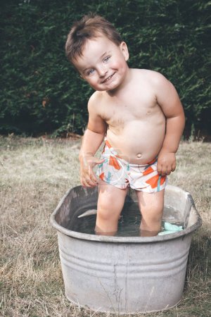 Photo for Little boy chilling in small retro sheet metal bathtub - Royalty Free Image