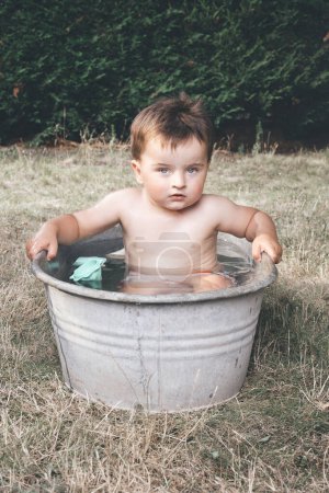 Foto de Niño pequeño que se enfría en una pequeña bañera de chapa retro - Imagen libre de derechos