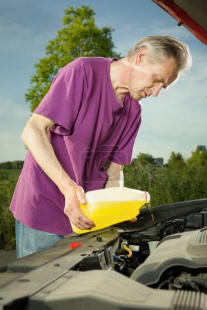 Photo for Older driver on longer trip topping up tank with washer fluid - Royalty Free Image