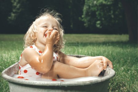Téléchargez les photos : Petite fille appréciant le bain dans la baignoire en tôle rétro dans le parc - en image libre de droit
