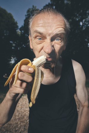 Téléchargez les photos : Laide homme de mauvaise condition manger de la banane fraîche après l'entraînement - en image libre de droit