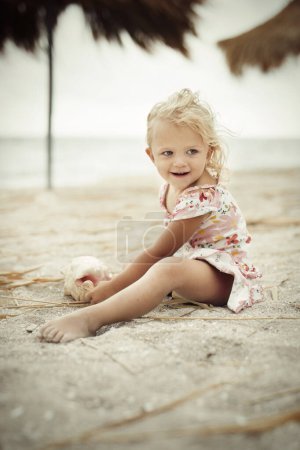 Foto de Chica de dos años y medio posando en la playa de mar con concha gigante - Imagen libre de derechos