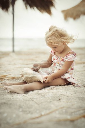 Foto de Chica de dos años y medio posando en la playa de mar con concha gigante - Imagen libre de derechos