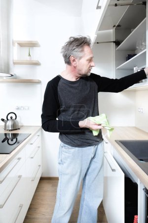 Photo for Older man cleaning kitchen space in apartment - Royalty Free Image