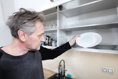 Téléchargez les photos : Homme plus âgé nettoyage de l'espace de cuisine dans l'appartement - en image libre de droit