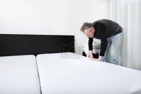 Téléchargez les photos : Homme plus âgé travaillant dans la chambre à coucher sur faire le lit - en image libre de droit