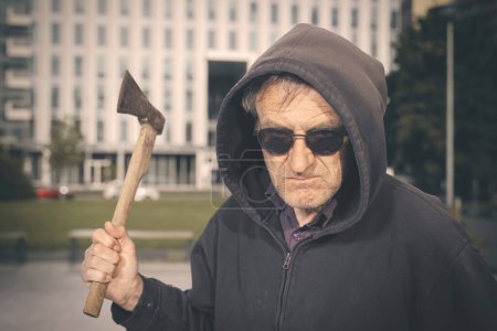 Photo for Aggressive older man with axe under the influence of drugs in park - Royalty Free Image