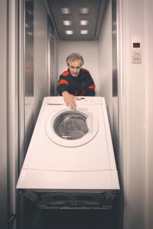 Foto de Hombre mayor en general moviendo la máquina de lavado en el carro con ascensor - Imagen libre de derechos