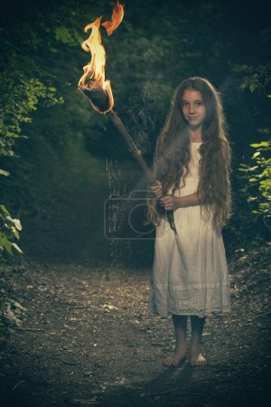 Foto de Niza joven posando en el bosque oscuro en ropa con antorcha en llamas - Imagen libre de derechos