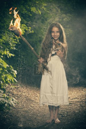 Photo for Nice young lady posing in dark forest in apparel with torch in flames - Royalty Free Image