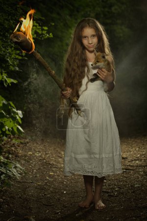Téléchargez les photos : Belle jeune femme posant dans la forêt sombre dans des vêtements avec torche en flammes - en image libre de droit