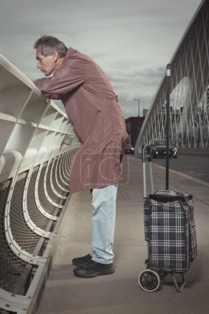 Photo for Senior citizen walking on city river bridge alone in daytime - Royalty Free Image