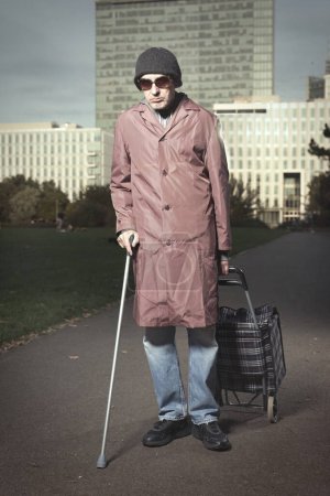 Foto de Ciudadano mayor caminando con carro de ruedas y palo en el parque de la ciudad - Imagen libre de derechos