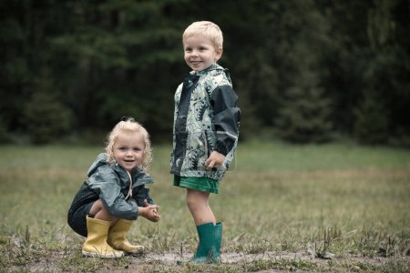 Photo for Kids playing on meadow in raincoats after raining - Royalty Free Image