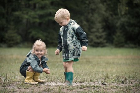Foto de Niños jugando en el prado con impermeables después de la lluvia - Imagen libre de derechos