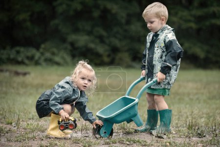 Téléchargez les photos : Enfants jouant sur la prairie en imperméables après la pluie - en image libre de droit