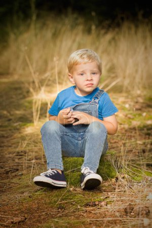 Foto de Niño pequeño vestido con jeans posando sobre muñón y sendero en el bosque - Imagen libre de derechos