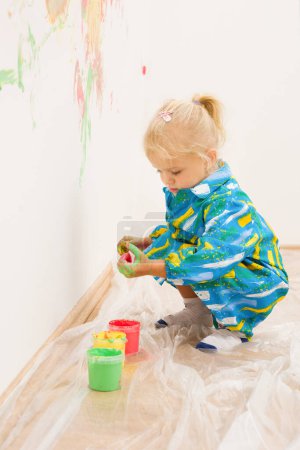 Foto de Niña rubia pintando a mano clara pared de la casa blanca - Imagen libre de derechos