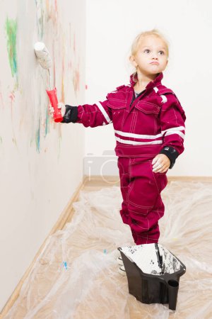 Foto de Niña rubia en overol reparando y pintando pared blanca - Imagen libre de derechos