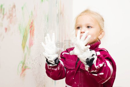 Foto de Niña rubia en overol jugando con el color blanco en la pared - Imagen libre de derechos