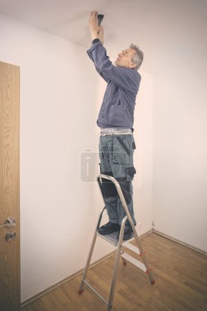 Foto de Hombre mayor reparando paredes y techo en apartamento vacío - Imagen libre de derechos