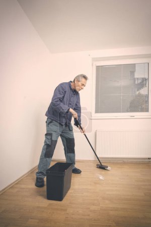 Photo for Older man cleaning and repairing floor in empty apartment - Royalty Free Image