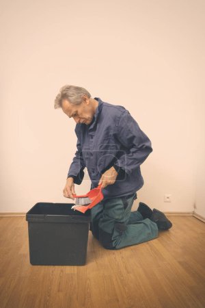 Foto de Hombre mayor limpiando y reparando piso en apartamento vacío - Imagen libre de derechos
