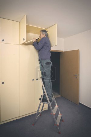 Foto de Hombre mayor desmonta gabinete en apartamento vacío listo para pintar - Imagen libre de derechos