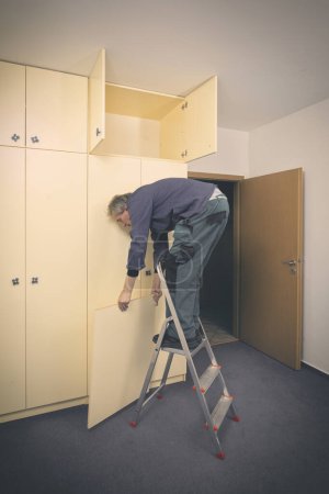 Téléchargez les photos : Homme plus âgé démonte armoire dans un appartement vide prêt pour la peinture - en image libre de droit