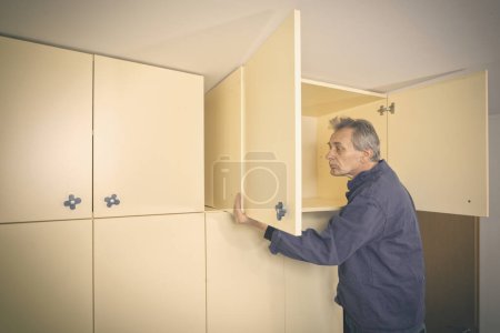 Photo for Older man disassembles cabinet in empty apartment ready for painting - Royalty Free Image