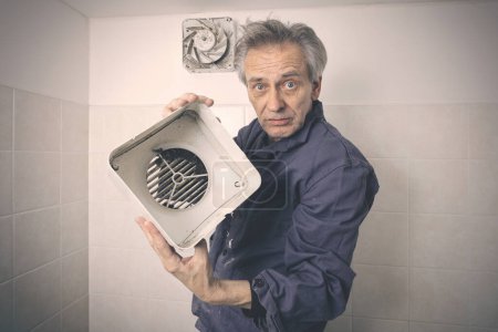 Téléchargez les photos : Homme plus âgé démontage et nettoyage ventilateur unité dans la salle de bain - en image libre de droit