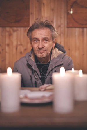 Photo for Senior citizen spending evening time in his small candle lit cottage shelter - Royalty Free Image