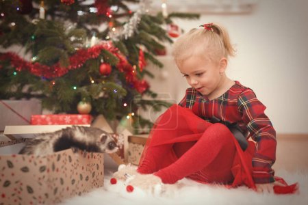 Photo for Girl in red at time of christmas day unpacking gifts near tree - Royalty Free Image