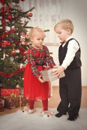 Foto de Pareja de niños en el momento del día de Navidad desempacando regalos cerca del árbol - Imagen libre de derechos