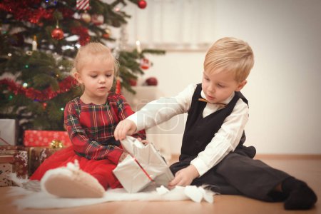 Photo for Couple of Children at time of christmas day unpacking gifts near tree - Royalty Free Image