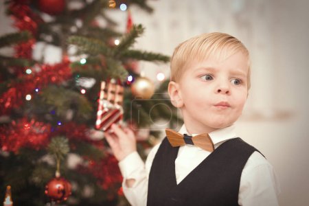 Téléchargez les photos : Garçon en robe formelle au moment du jour de Noël déballer des cadeaux près de l'arbre - en image libre de droit