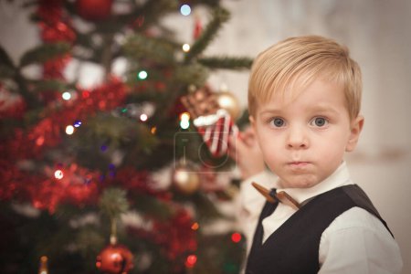 Foto de Niño en vestido formal en el momento del día de Navidad desempacar regalos cerca del árbol - Imagen libre de derechos