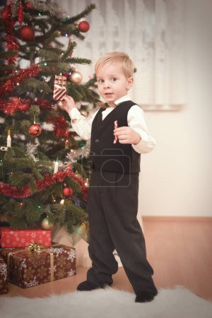 Foto de Niño en vestido formal en el momento del día de Navidad desempacar regalos cerca del árbol - Imagen libre de derechos