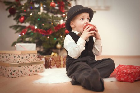 Foto de Niño en sombrero de jugador de bolos en el momento del día de Navidad desempacar regalos cerca del árbol - Imagen libre de derechos