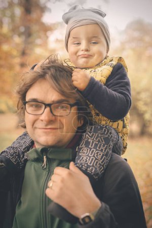 Photo for Man carrying his son on the shoulders in late fall park - Royalty Free Image