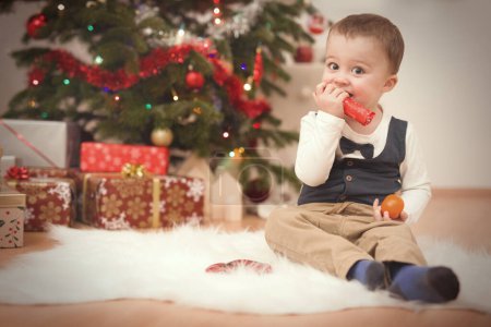 Photo for Little boy at time of christmas day unpacking gifts near tree - Royalty Free Image