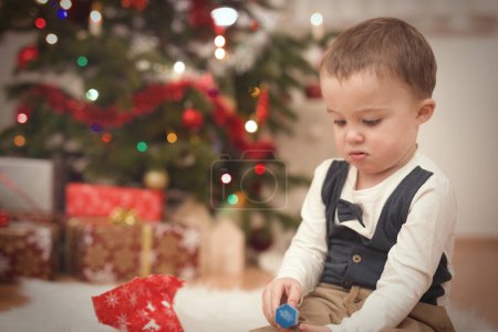 Photo for Little boy at time of christmas day unpacking gifts near tree - Royalty Free Image
