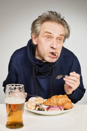 Photo for Older man eating sweet pastry and cakes as a meal in studio - Royalty Free Image