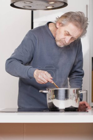 Téléchargez les photos : Homme plus âgé dans la cuisine spaghetti bouillant pour la réception classique - en image libre de droit