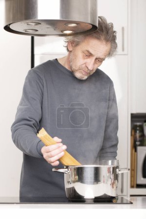 Photo for Older man in kitchen boiling spaghetti for classic receipe - Royalty Free Image