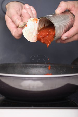 Téléchargez les photos : Homme plus âgé dans la boîte d'ouverture de la cuisine de sauce tomate pour spaghetti - en image libre de droit