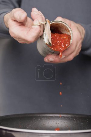 Téléchargez les photos : Homme plus âgé dans la boîte d'ouverture de la cuisine de sauce tomate pour spaghetti - en image libre de droit