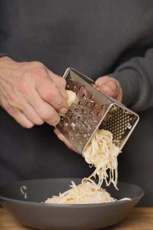 Téléchargez les photos : Homme plus âgé en fromage râpé de cuisine pour spaghettis à la viande hachée, tomates et gouda - en image libre de droit