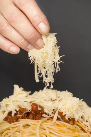 Foto de Hombre mayor en cocina rallando queso para espaguetis con carne picada, tomates y gouda - Imagen libre de derechos